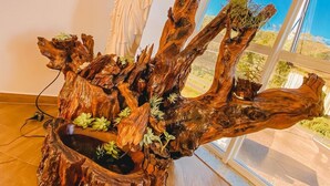 A wooden sculpture with branches and greenery, placed in a room with a large window and a sign on the wall. - Gringo Hotel (Erval Velho)