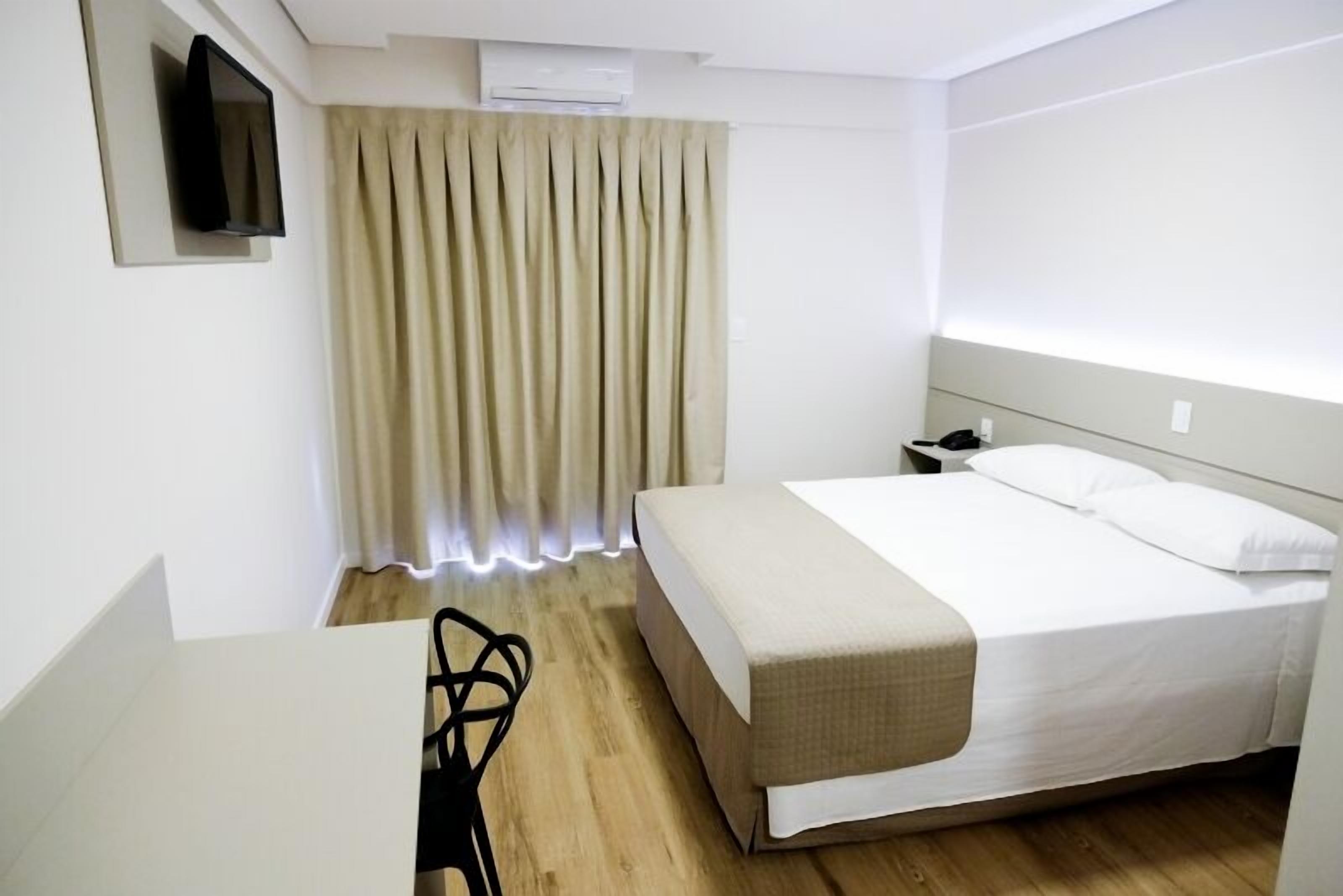 A hotel room with a bed, bedside table, chair, and a TV mounted on the wall.