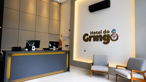 A hotel reception area with a reception desk, two grey chairs, and a wall-mounted sign reading "Hotel do Gringo". - Gringo Hotel (Erval Velho)