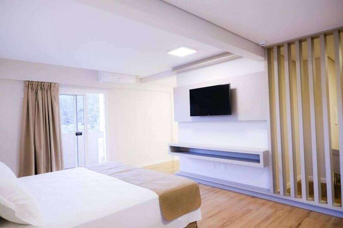 A modern hotel room with a bed, a TV mounted on the wall, and a sliding door.