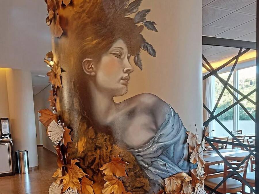 Un mural con una mujer rodeada de hojas y ramas otoñales.