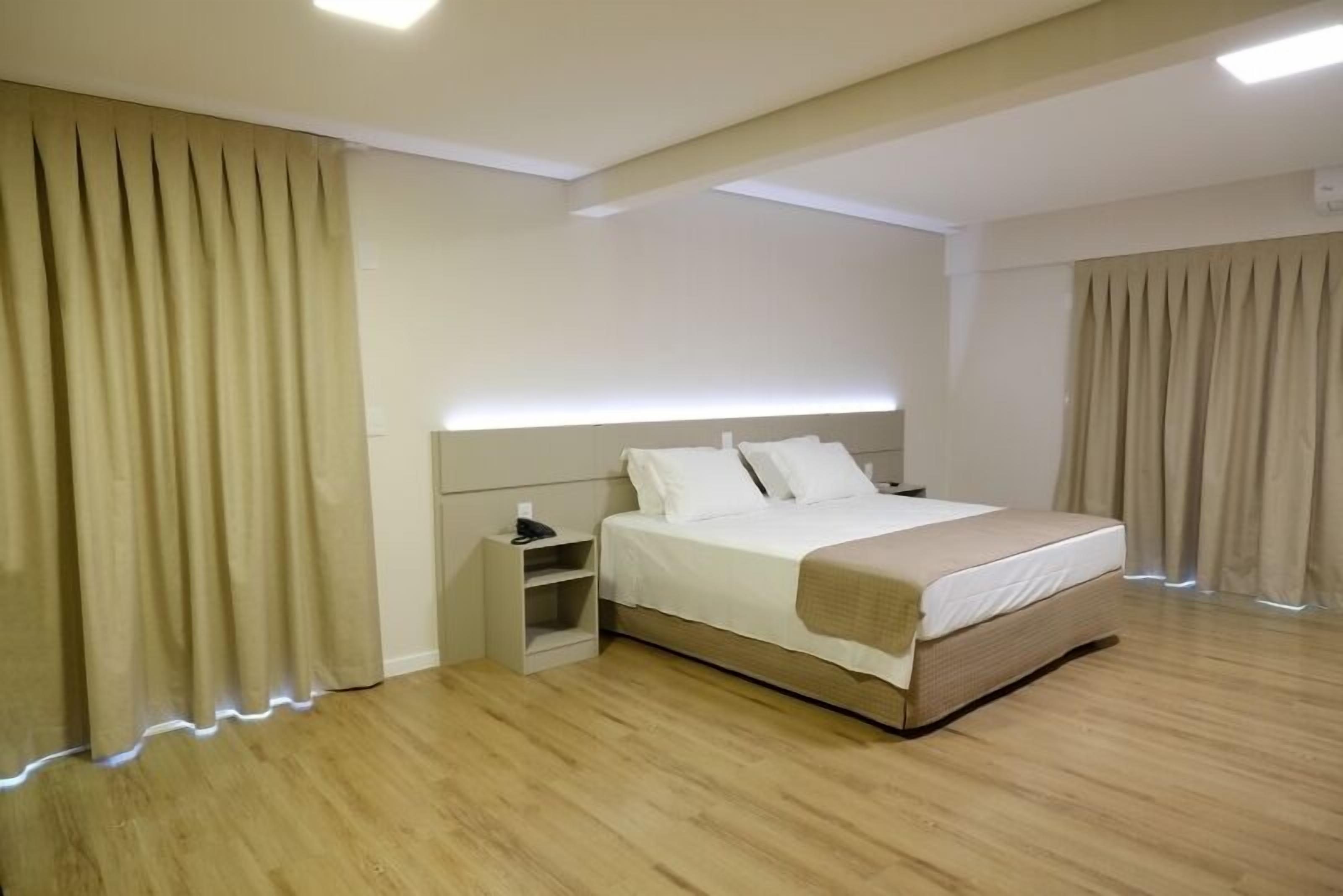 Une chambre d’hôtel moderne avec un grand lit, une table de chevet et une tête de lit dotée d’un éclairage intégré.