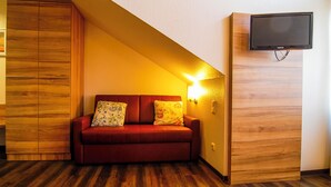 A room with a wooden wardrobe, a red sofa with patterned cushions, and a mounted television. - Adolph*s.hotel (Cologne)