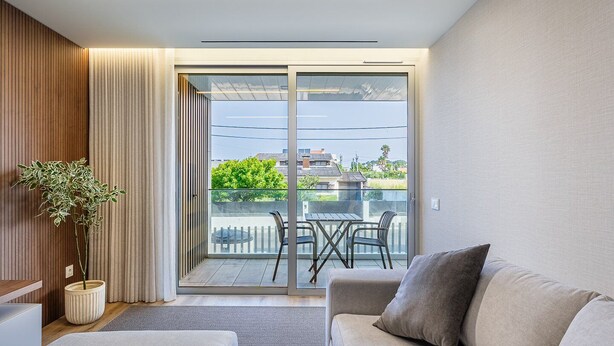 A modern living room with a sofa, a potted plant, and a sliding glass door leading to an outdoor patio with a table and chairs. - GuestReady - Beach and Pool Escape in Gaia (Vila Nova de Gaia)