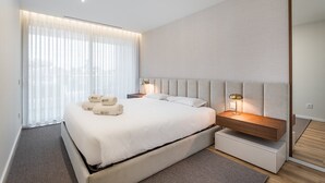 A modern hotel room with a large bed, a nightstand with a lamp, and a large mirror. - GuestReady - Beach and Pool Escape in Gaia (Vila Nova de Gaia)