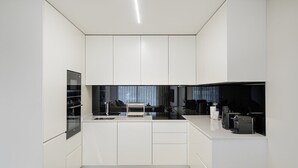 A modern kitchen with white cabinetry, a black countertop, and a built-in oven. - GuestReady - Beach and Pool Escape in Gaia (Vila Nova de Gaia)