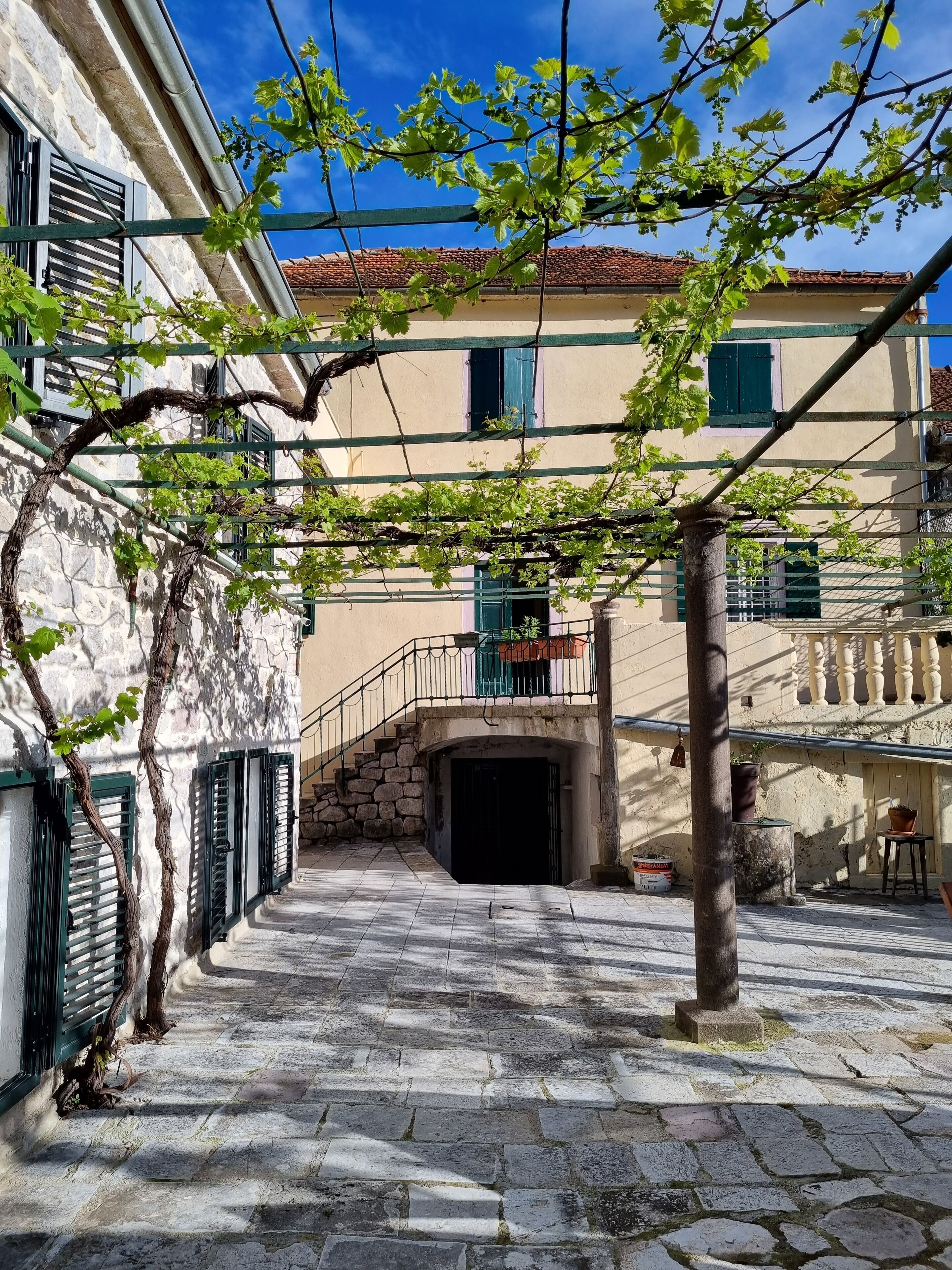 Un estrecho callejón empedrado con un edificio de fachada de piedra y contraventanas verdes.