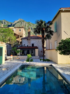 A pool area with stone tiles, a stone building with a tiled roof, and a mountain backdrop. - Old bakery house (Risan)