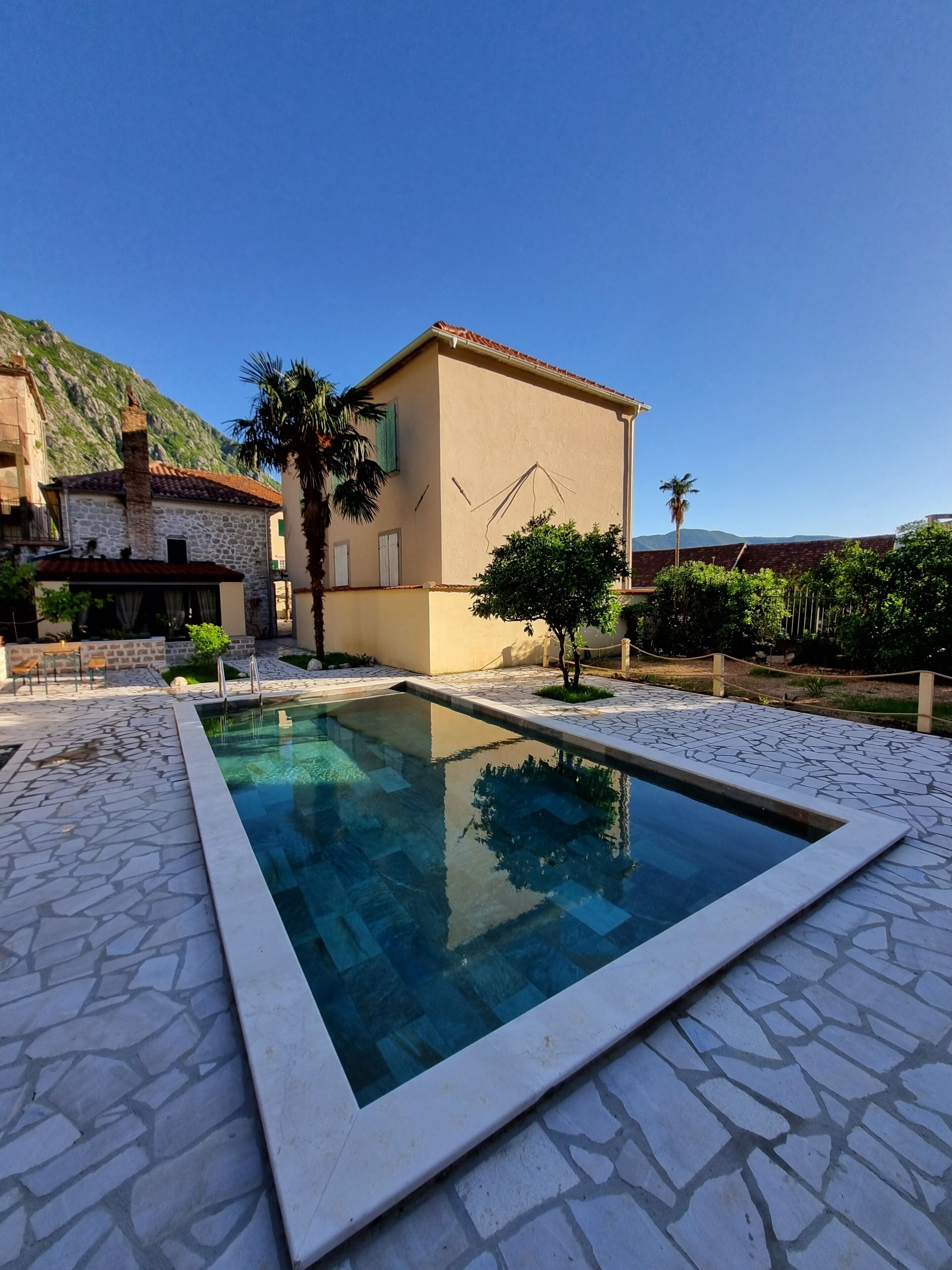 A swimming pool with stone tiles, a stone building, and a mountain in the background.