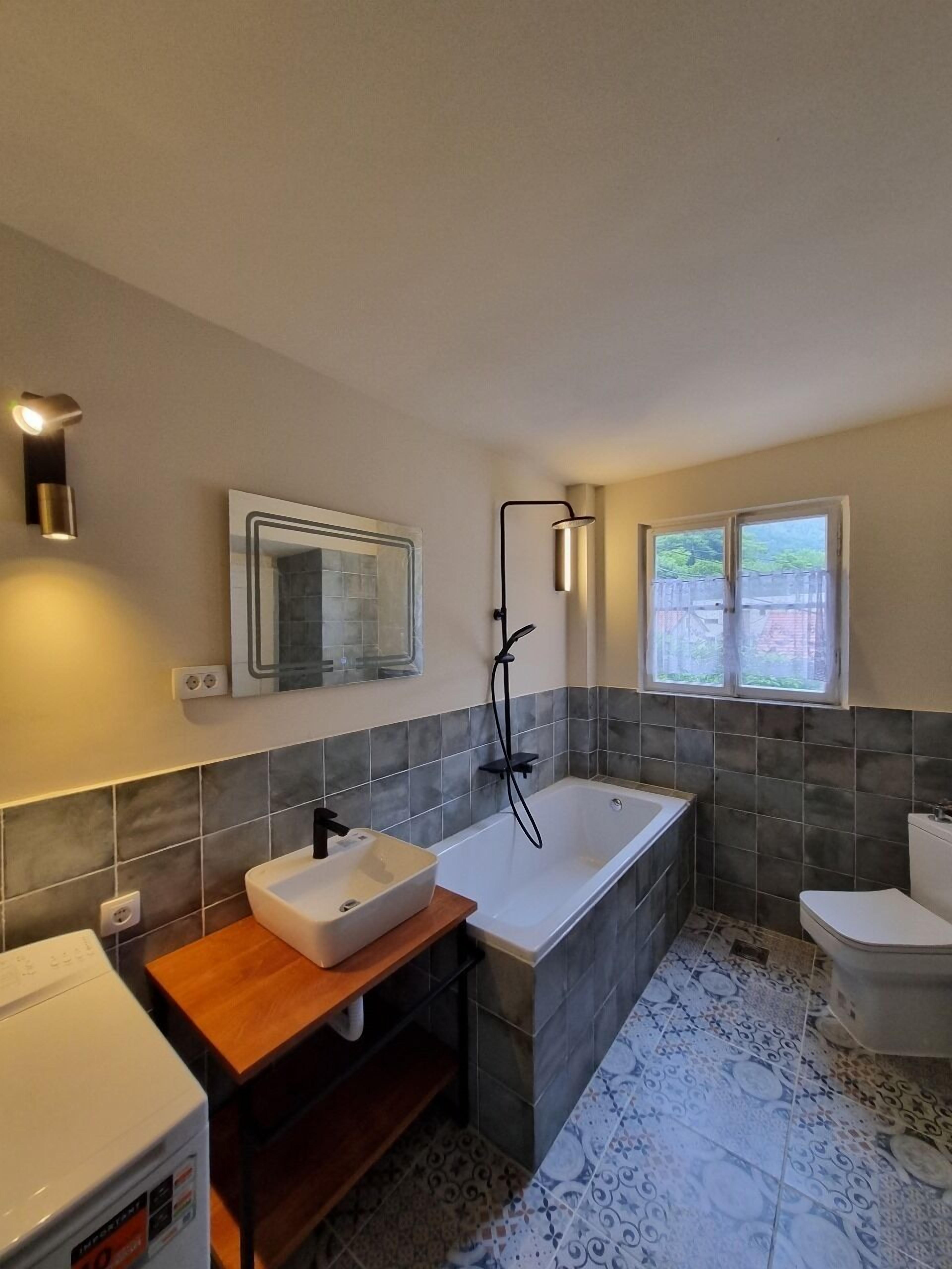 A modern bathroom with a freestanding bathtub, a large mirror, and a window providing natural light.