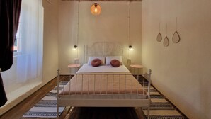 A bedroom with a wooden ceiling, a bed with patterned bedding, two bedside tables, and a hanging light fixture. - Old bakery house (Risan)
