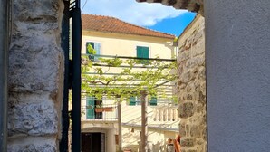 A narrow stone pathway leading to a building with a tiled roof and green shutters. - Old bakery house (Risan)