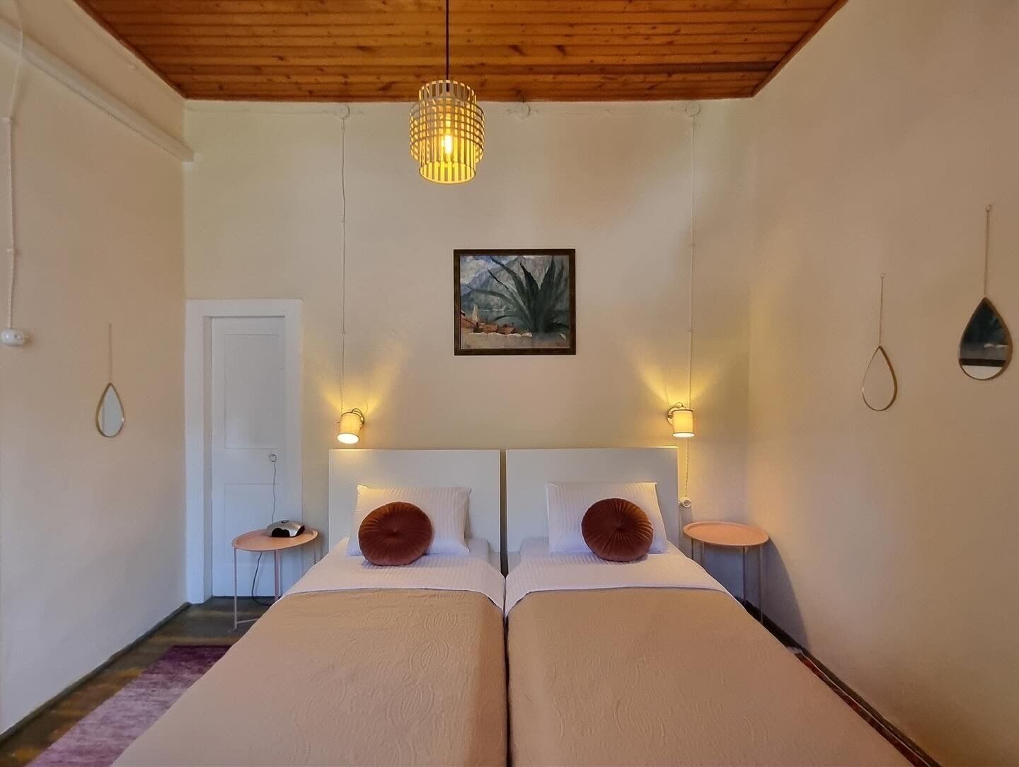 Un lit double avec deux oreillers, un luminaire suspendu, une petite table ronde et une porte.
