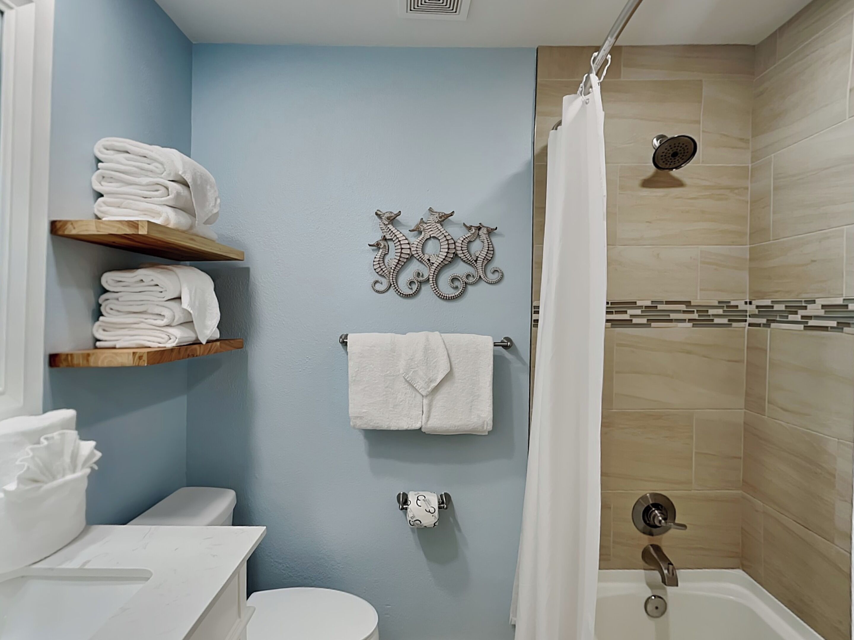 A bathroom with a toilet, a sink, a shower with a curtain, and towel racks with folded towels.