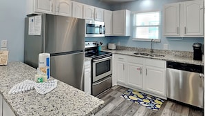 Una cocina moderna con armarios blancos, electrodomésticos de acero inoxidable, encimeras de granito y una araña.