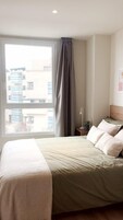 Ein Schlafzimmer mit einem Bett, einem Nachttisch, einer Lampe und einem Fenster mit Vorhängen.