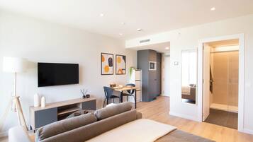 A modern hotel room with a sofa, a TV, a desk, and a shower area.