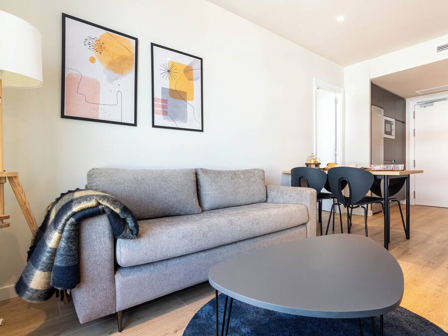 Una sala de estar moderna con un sofá gris, una mesa redonda y un comedor con sillas.