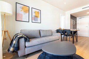 Ein modernes Wohnzimmer mit grauem Sofa, einem runden Tisch und einem Essbereich mit Stühlen.