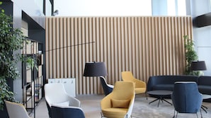 A modern lobby with contemporary chairs, a wooden slatted wall, and a large window. - Welco Valdebebas (Madrid)