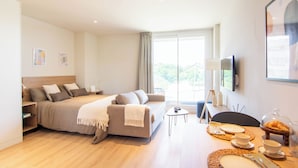 A modern hotel room with a large bed, a sofa, a dining table with breakfast items, and a TV on the wall. - Welco Valdebebas (Madrid)