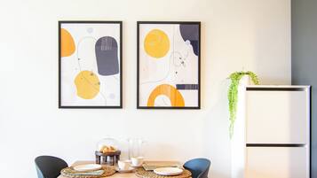 Un comedor con una mesa de madera, sillas negras y dos cuadros abstractos en la pared.