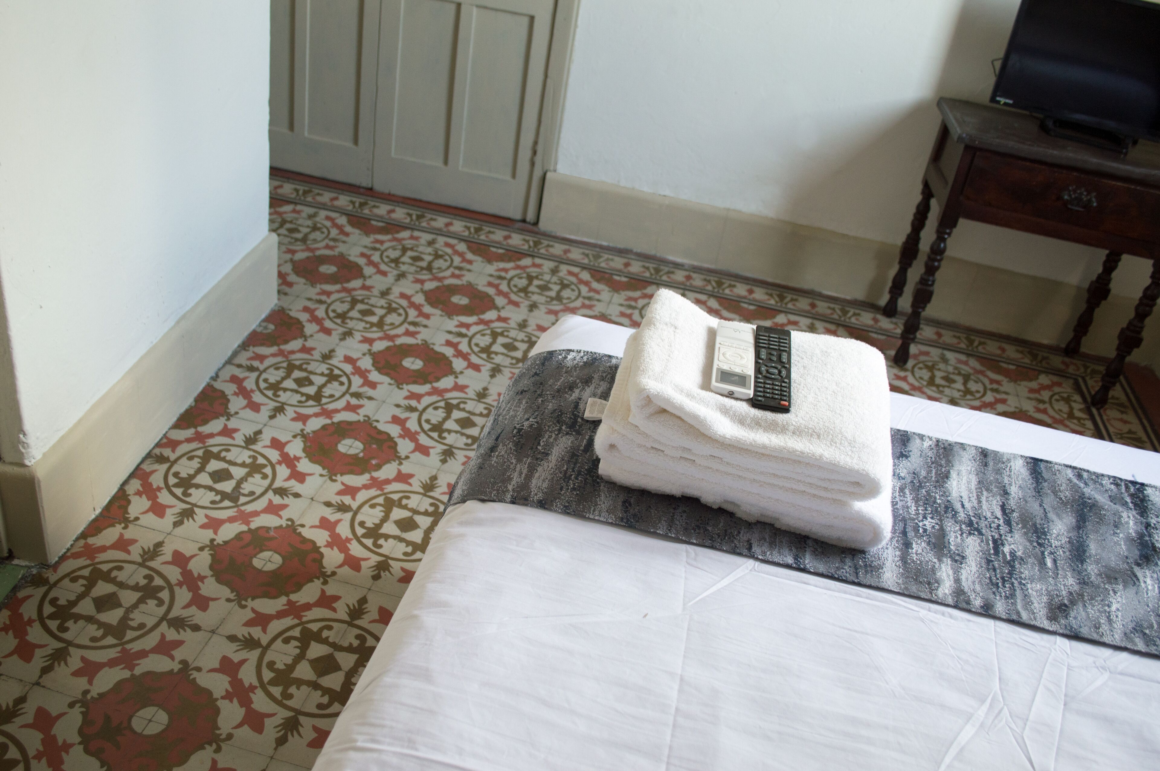 A hotel room with a bed, a folded towel, and a remote control on the bed.
