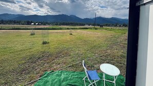 Un balcon donnant sur un champ verdoyant, des montagnes et un ciel partiellement nuageux.