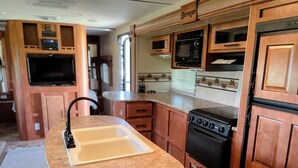 Cocina compacta de autocaravana con pileta, estufa, microondas y un televisor al fondo.