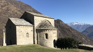Igreja de pedra com uma cruz, ao fundo montanhas.