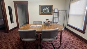 Une salle de conférence avec une table en bois, deux chaises grises, un tableau encadré au mur et une fenêtre avec des stores.