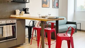 Une cuisine compacte équipée d’un four à micro-ondes, d’une machine à café et d’un coin repas avec des chaises rouges et un canapé bleu clair.