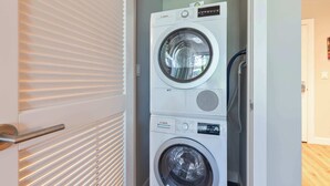 A stacked washer and dryer unit in a laundry room with a door and blinds.