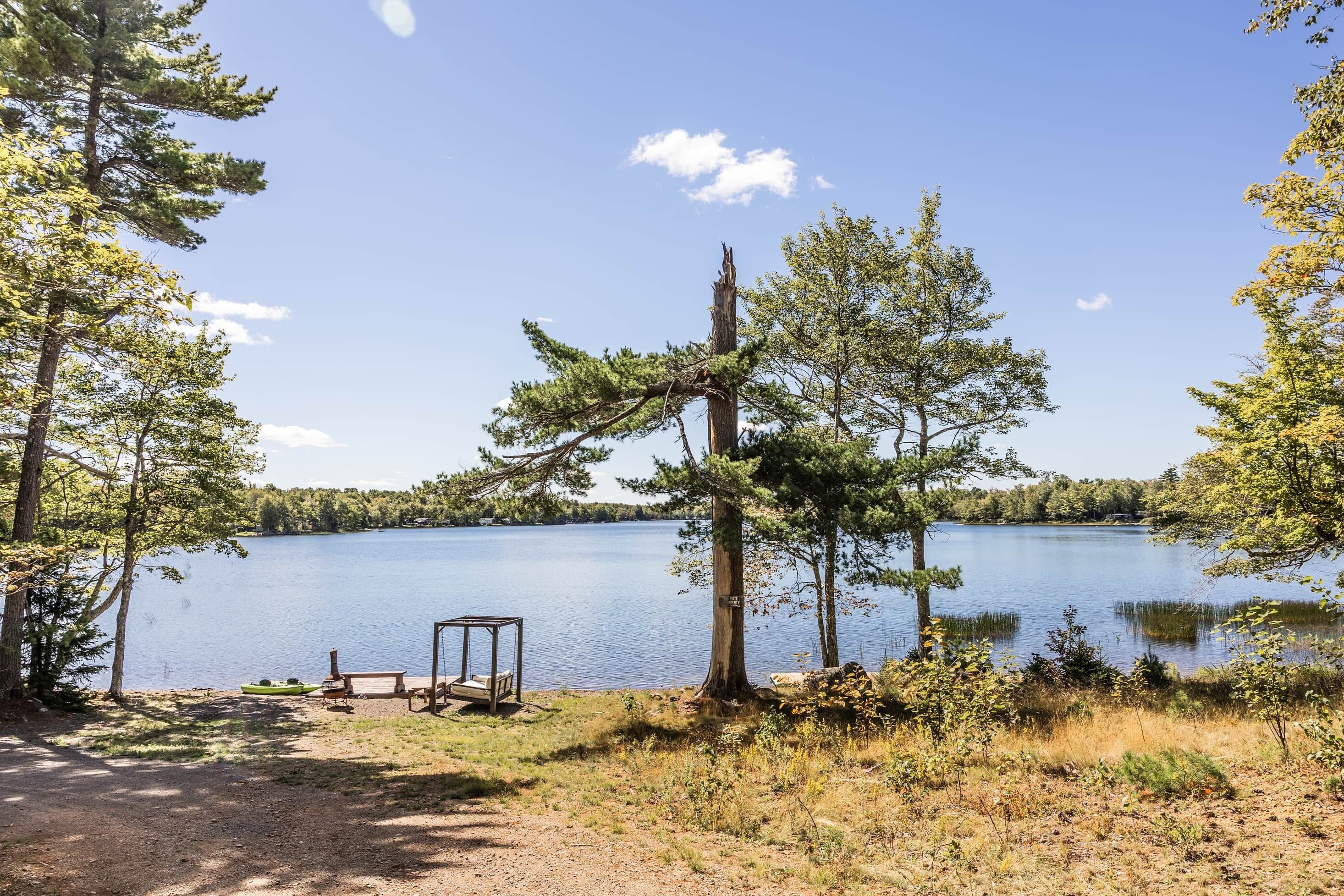 Un terrain de camping au bord du lac, avec un banc en bois, un petit bateau et une table de pique-nique.