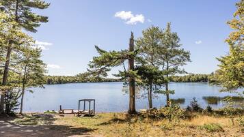 Un terrain de camping au bord du lac, avec un banc en bois, un petit bateau et une table de pique-nique.