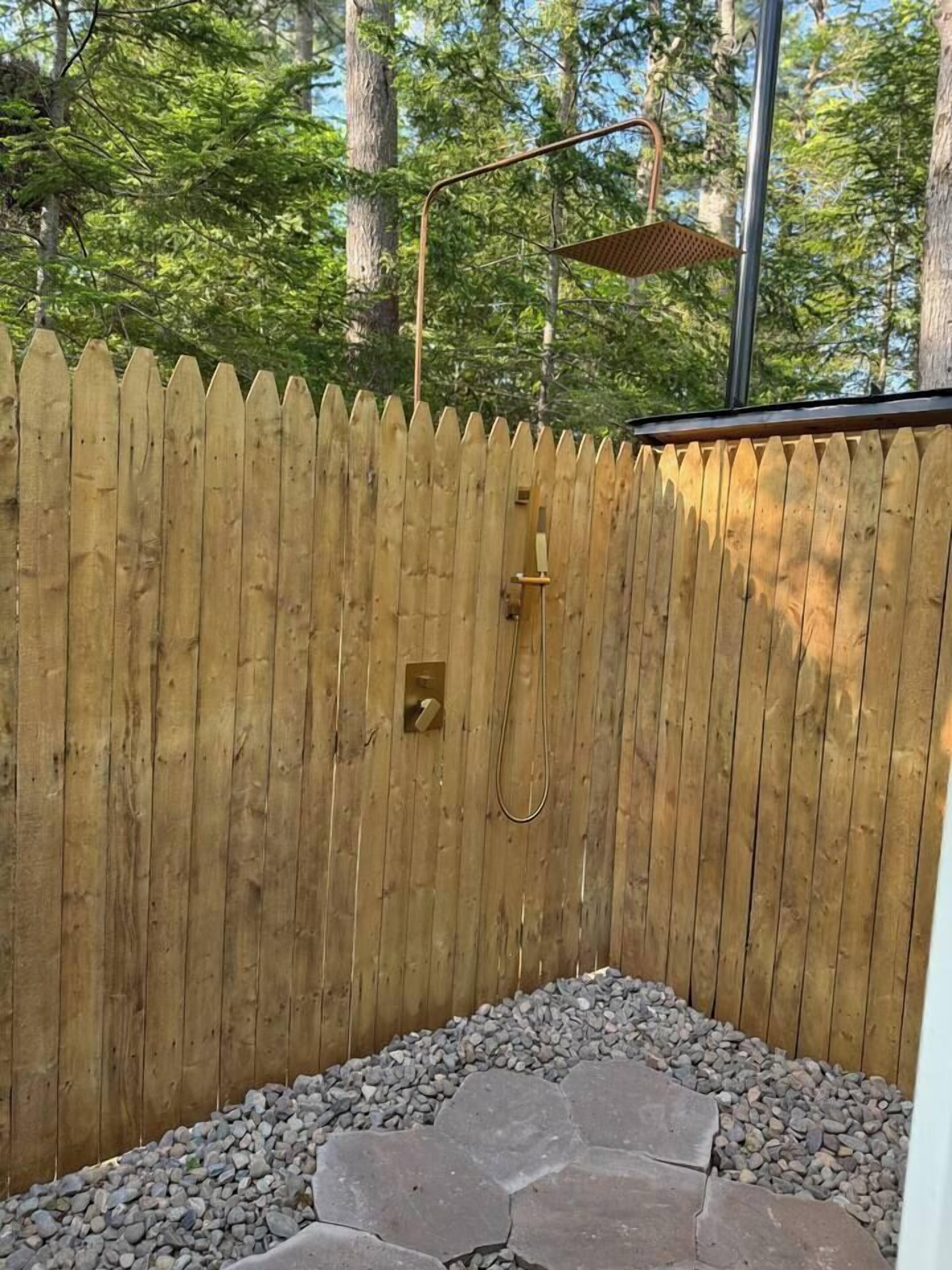 A wooden fence with a built-in shower area, surrounded by a stone pathway.