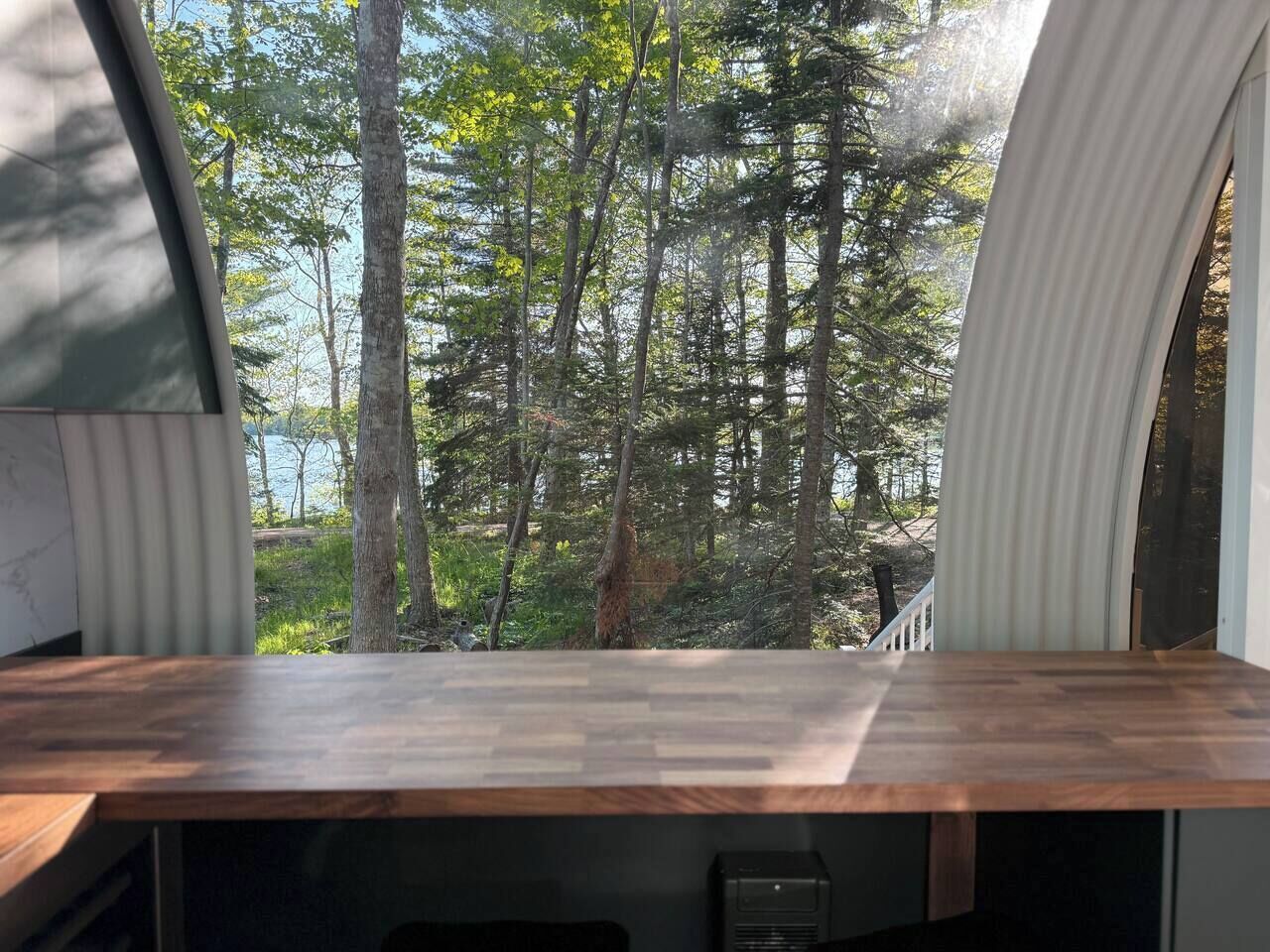 Ein modernes Wohnmobil-Interieur mit einem Holztisch und Blick auf einen Wald durch die Fenster.