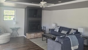 A modern living room with a grey sofa, a fireplace, and a ceiling fan.