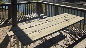 A wooden deck with a table and benches overlooking a river and forest.