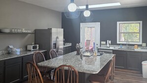 A modern kitchen with dark cabinetry, a central island with bar stools, pendant lighting, and a view through a window.