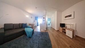 A modern living room with a sofa, a TV stand, and a kitchen in the background. - Praia da Rocha River View 740 (Portimão)