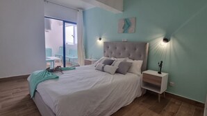 A bedroom with a large bed, two bedside tables, a nightstand, a window with a view, and a wall-mounted light fixture. - Praia da Rocha River View 740 (Portimão)
