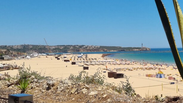 A beach with tents and beachgoers, a clear sky, and a distant lighthouse. - Praia da Rocha River View 740 (Portimão)