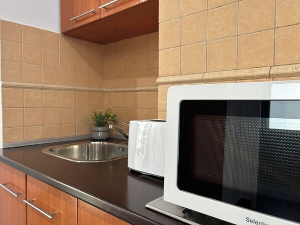 A kitchen with a white microwave, a stainless steel sink, and wooden cabinets.