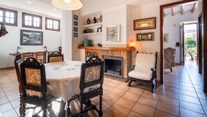 Une salle à manger avec une table ronde, des chaises, une cheminée et un couloir menant à un espace extérieur.