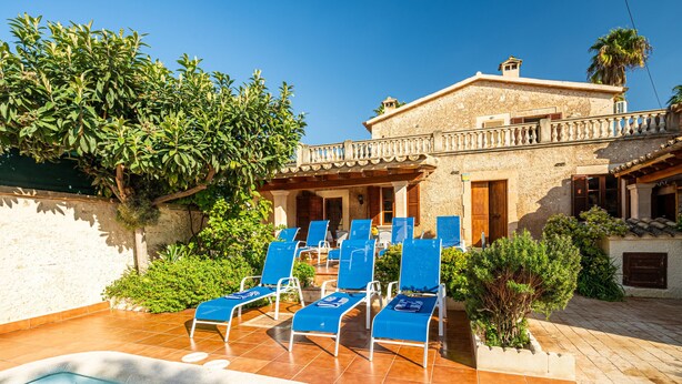Un espace piscine doté de chaises longues bleues et d’un jacuzzi, le tout entouré d’un bâtiment en pierre avec un balcon.