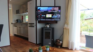 A modern kitchen with white cabinets, a built-in microwave, and a coffee maker. A flat-screen TV mounted above the kitchen counter displays various channels. - Palmocolodge Lodge - Jocomo Parc a nice family campground with many facilities (Lanaken)