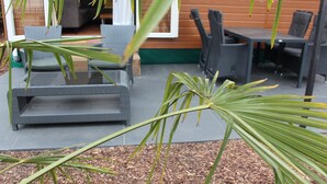 An outdoor seating area with wicker furniture, a wooden wall, and a palm plant in the foreground. - Palmocolodge Lodge - Jocomo Parc a nice family campground with many facilities (Lanaken)