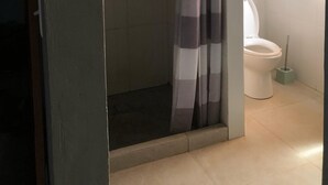 A bathroom with a shower, toilet, and a small shelf with toiletries.