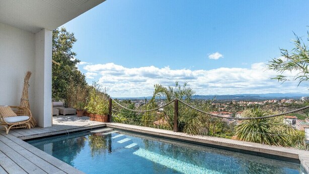 An infinity pool with a view of a cityscape, wooden deck, wicker furniture, and potted plants. - House 5p with garden in the heart of Saint-Raphaël (Saint-Raphaël)